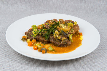 Large stews of beef meat with vegetables in a large white plate on a gray background