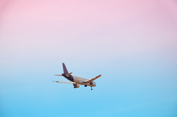 Large plane flies in the evening sunset sky, romantic painted sky and airplane silhouette with clouds over Lisbon in Portugal.