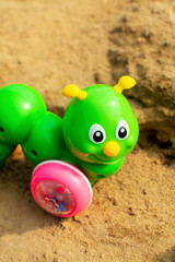 Fototapeta na wymiar Bright green caterpillar toy in the sandbox. Funny children toy.
