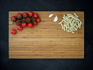cherry tomato, garlic and fusilli on cutting wooden board