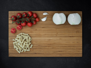 cherry tomato, onion, garlic and fusilli on cutting wooden board