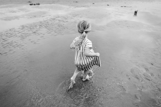 little girl runs on the beach in monochrome image in dress with stripes