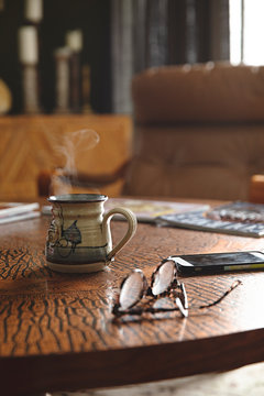 Hot coffee / tea in a retro mug with steam in interior setting with glasses on coffee table