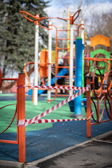 Fototapeta premium Covid-19 coronovirus infection pandemic. Fenced playground. The entrance is wound with warning tape in white and red. Everyone is sitting at home. Empty area without children.