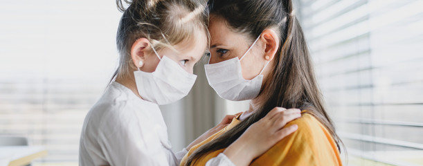 Mother and child with face masks indoors at home, Corona virus and quarantine concept.