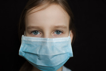 Coronavirus Covid-19 outbreak. Little blonde girl with blue eyes wearing disposable mask for protection of virus on black background in studio. Personal protective equipment concept