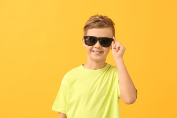 Cute little boy with sunglasses on color background
