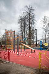 Fototapeta premium Empty playground in a city park, fenced with warning tapes of red and white. Coronavirus pandemic covid-19 in the world. Stay at home