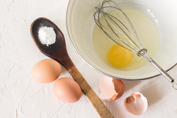 one broken egg in a Cup with a whisk and two whole eggs with a shell and a wooden spoon with baking powder
