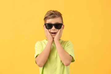 Surprised little boy with sunglasses on color background