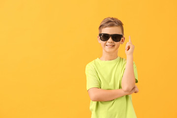 Cute little boy with sunglasses and raised index finger on color background