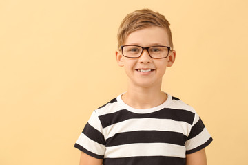 Cute little boy with eyeglasses on color background