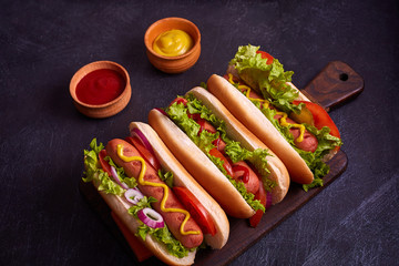 Hot dogs with sausage, fried onion, coriander leaves, cheese sauce and mustard, served on baking paper over black concrete texture background. Fast food. Top view, copy space