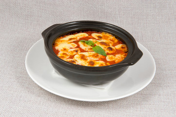 Tomato soup with cheese in a black bowl with a white plate on a gray background