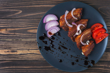 Fried pork belly with sauce and onions in a dark gray plate on a wooden tabletop
