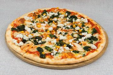 Pizza with traditional cheese and mozzarella, as well as tomato, canned sweet corn, spinach on a wooden plate on a gray background