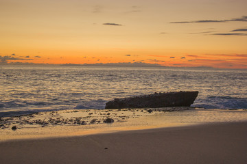 Beautifully colored Laguna Beach sunset over the ocean with Catalina Island in background and Aliso rock silhouetted in the foreground and wet sand reflecting the sunlight and colors.