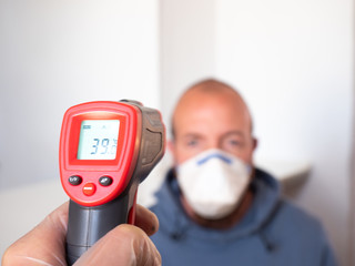 Taking a man's temperature with an infrared meter. High fever, symptom, disease.