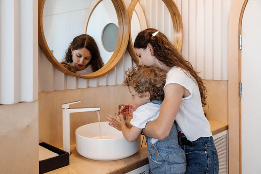 Baby washing hands in bathroom with help of mother