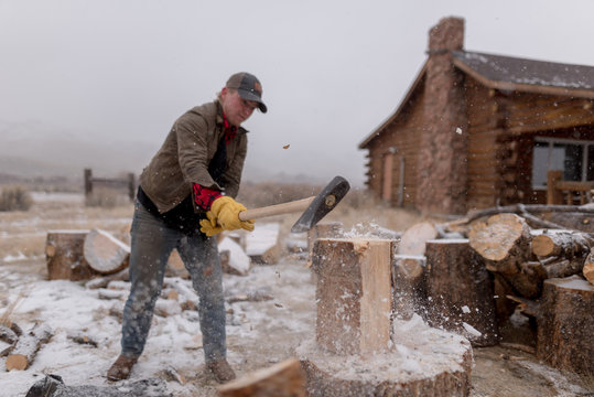 Ranch hand chopping wood in a snowstorm by a cabin