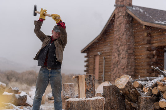 Ranch hand chopping wood in a snowstorm by a cabin