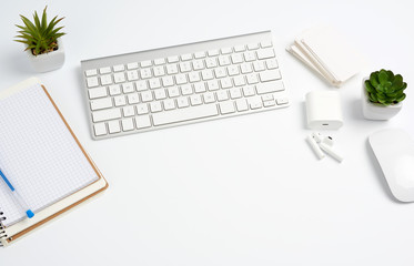 White wireless keyboard, a stack of notebooks, green plants in pots and a mouse, workplace of a freelancer