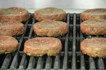 Raw hamburger patties organized on hot char broiler grill