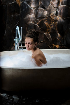 Attractive unusual girl takes a hot bath. Beautiful bathroom with large stone bath