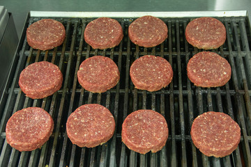 Top view of Raw hamburger patties sitting on hot char broiler grill