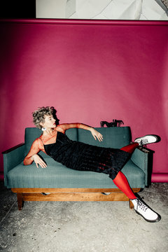 Fashion girl portrait lying in red tights on a vintage sofa on pink background