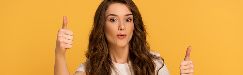 Naklejka premium panoramic shot of beautiful surprised woman showing thumbs up isolated on yellow