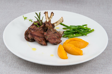 Roasted meat on a rib, stewed garlic arrows, baked pumpkin on a large round plate on a gray background