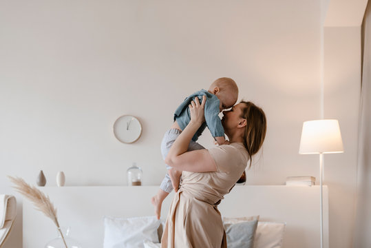 Mother in beige dress holding daughter by hands.