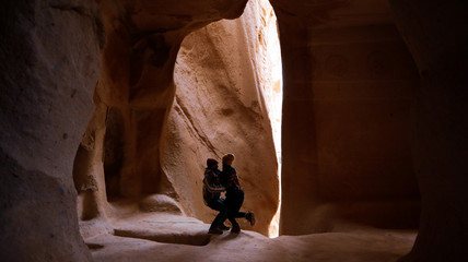 Travel couple standing into the cave surrounded by rock formations at Zelve Valley in Cappadocia, Turkey - Powered by Adobe