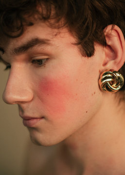 Portrait of a queer guy with curly hair and golden earrings who blushes