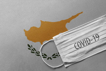 Face Medical Surgical White Mask with COVID-19 inscription lying on Cyprus National Flag. Coronavirus in Cyprus