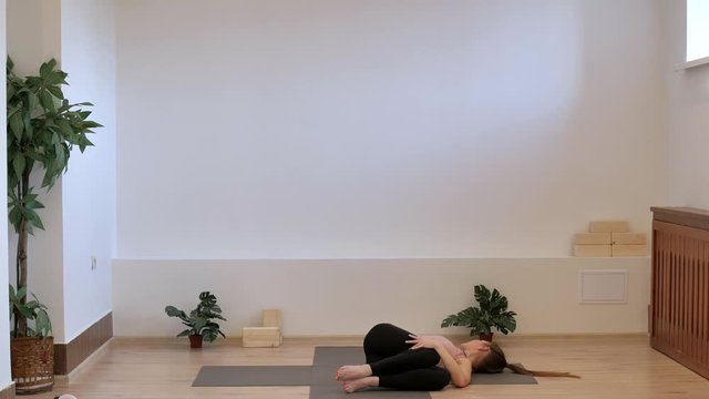 A yoga teacher in a Pilates studio on a yoga mat shows the correct execution of twisting the back and lower back in a twisted belly pose. Jathara parivartanasana.
