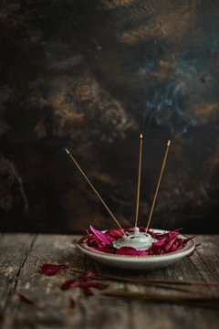Incense sticks burning inside porcelain holder in bowl filled with scarlet peony petals