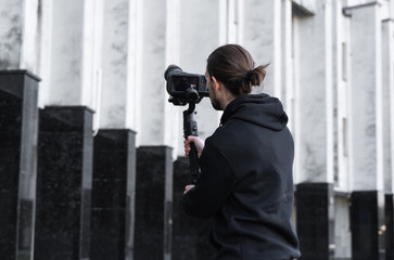 Young Professional videographer holding professional camera on 3-axis gimbal stabilizer. Pro equipment helps to make high quality video without shaking. Cameraman wearing black hoodie making a videos. © Volodymyr_sh