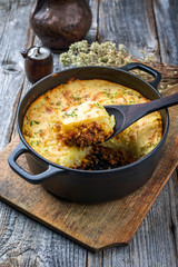 Traditional English shepherd pie offered as closeup in a Dutch oven on a wooden board