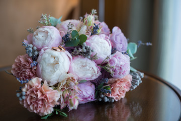 beautiful bridal bouquet of the bride, made of pink peonies and powdery-colored carnations, on a shiny table, against the background of an armchair, in a chic light interior of a hotel