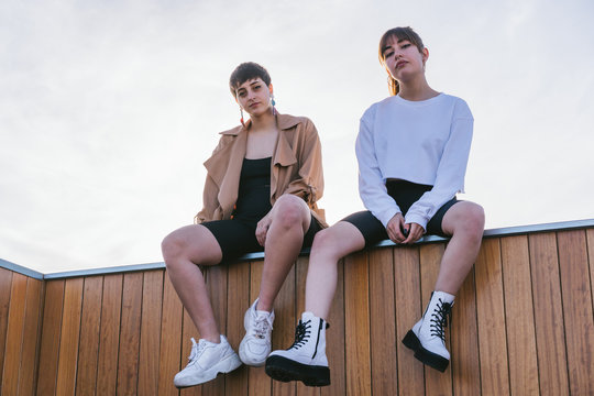 Two Confident Girlfriends Sitting On a Wooden Wall.