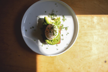 Avocado with poached egg on a plate in a rectangle of sunlight, minimalistic concept, place for an inscription.