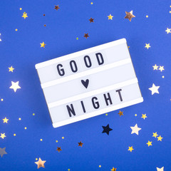 Good night written on a decorative panel on a blue background among the stars. Top view, flat lay.