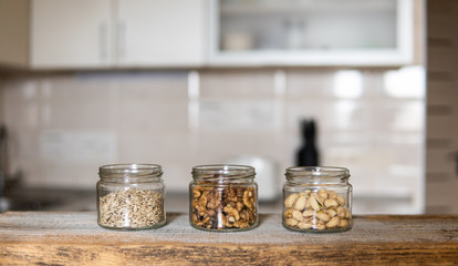 Sunflower seeds, walnut and pistachio in a jars which standing on a white vintage table with a kitchen on background. Nuts is a healthy vegetarian protein and nutritious food. Nuts on rustic old wood.