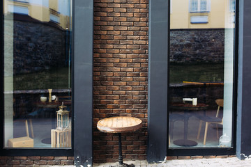 Small wooden table on the outside modern terrace of the wine restaurant. There are two panoramic windows and decorative materials on the background: brick and metal. Table in front of a cafe