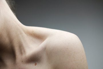 woman with no face exposing her right shoulder and collar bone with pale skin and freckles