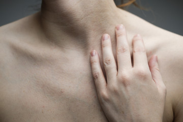 Woman with no face touching her hand to her neck and exposing her collar bones and décolletage; pale skin, freckles and moles