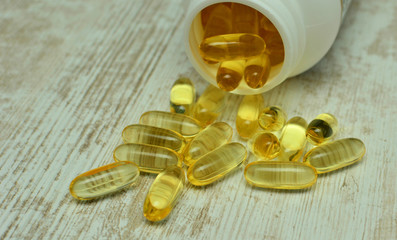 Fish oil capsules with omega 3 and vitamin D in a plastic bottle on a shiny texture with sun beams,...