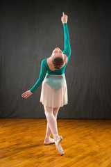 Ballerina in green leotard and skirt, dancing in the studio.